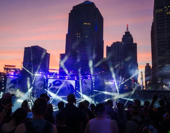 Sunset over Detroit skyline with stage lights and crowd silhouettes at Hart Plaza