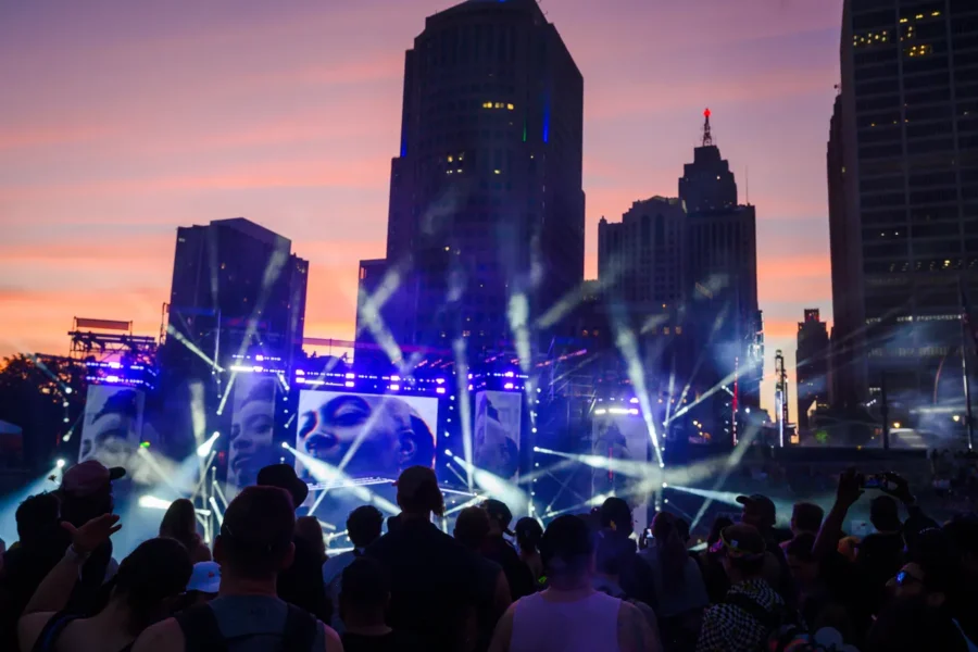 Sunset over Detroit skyline with stage lights and crowd silhouettes at Hart Plaza